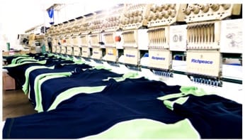 Escena 5: Máquinas rotulando logos en uniformes — SOGAM conecta al cliente directamente con la producción.